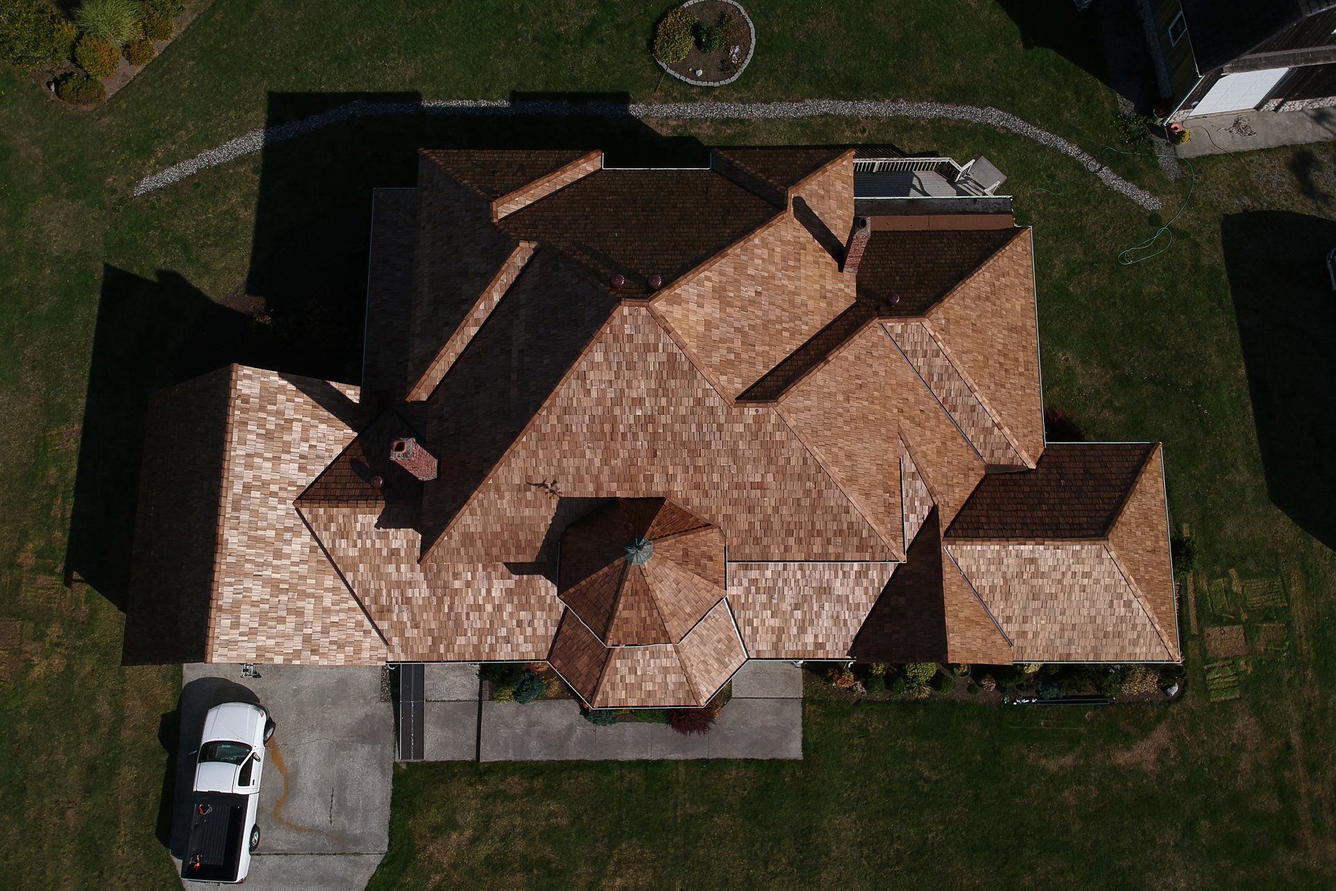 Aerial view of a house with a tan shingled roof, driveway with a white car, and green lawn.