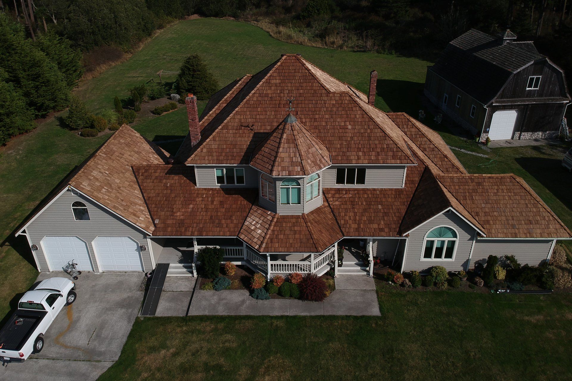 Aerial view of a large house with a red-tiled roof, white garage, and green lawn.