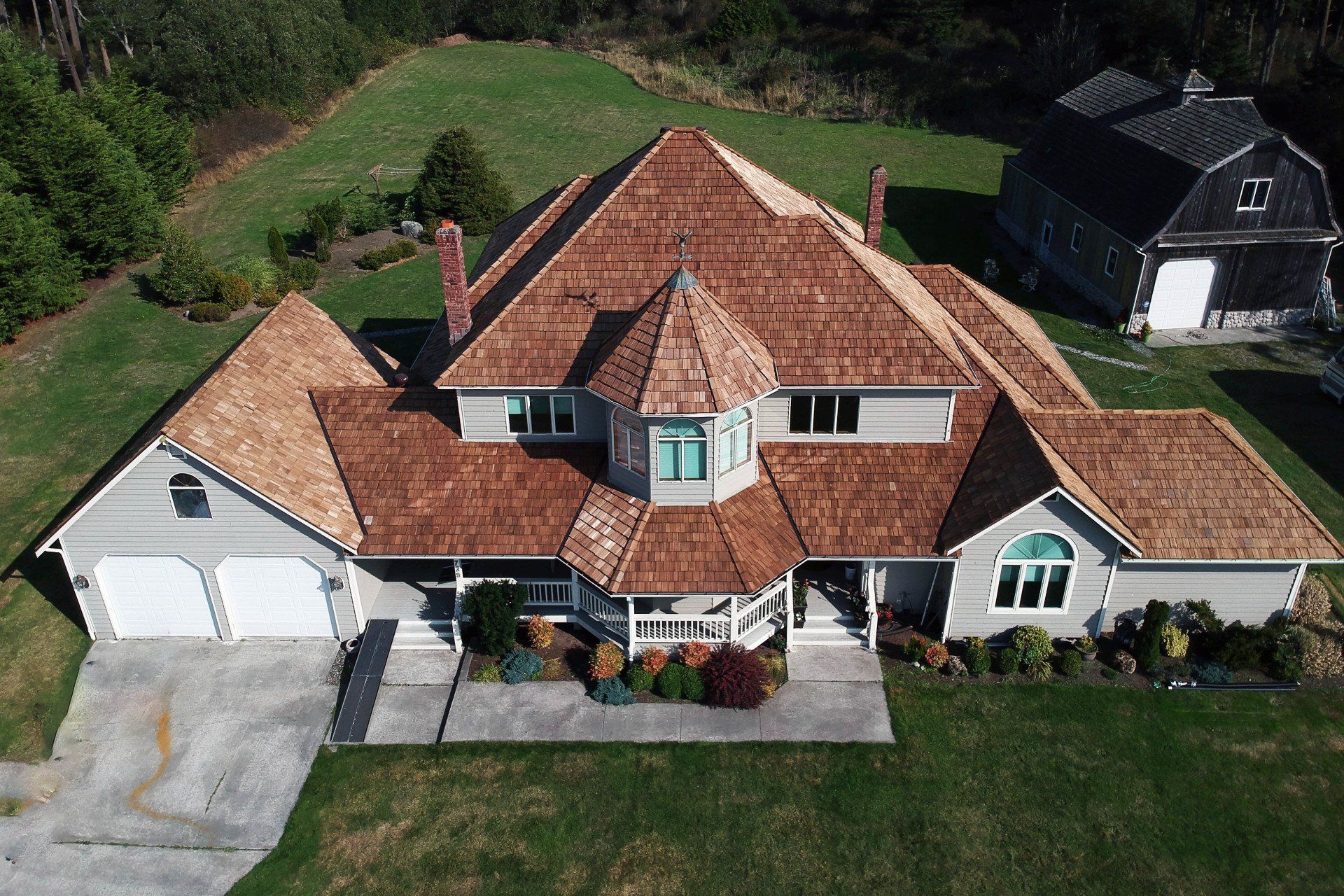 Aerial view of a large tan house with a red-tile roof, white garage, and green lawn