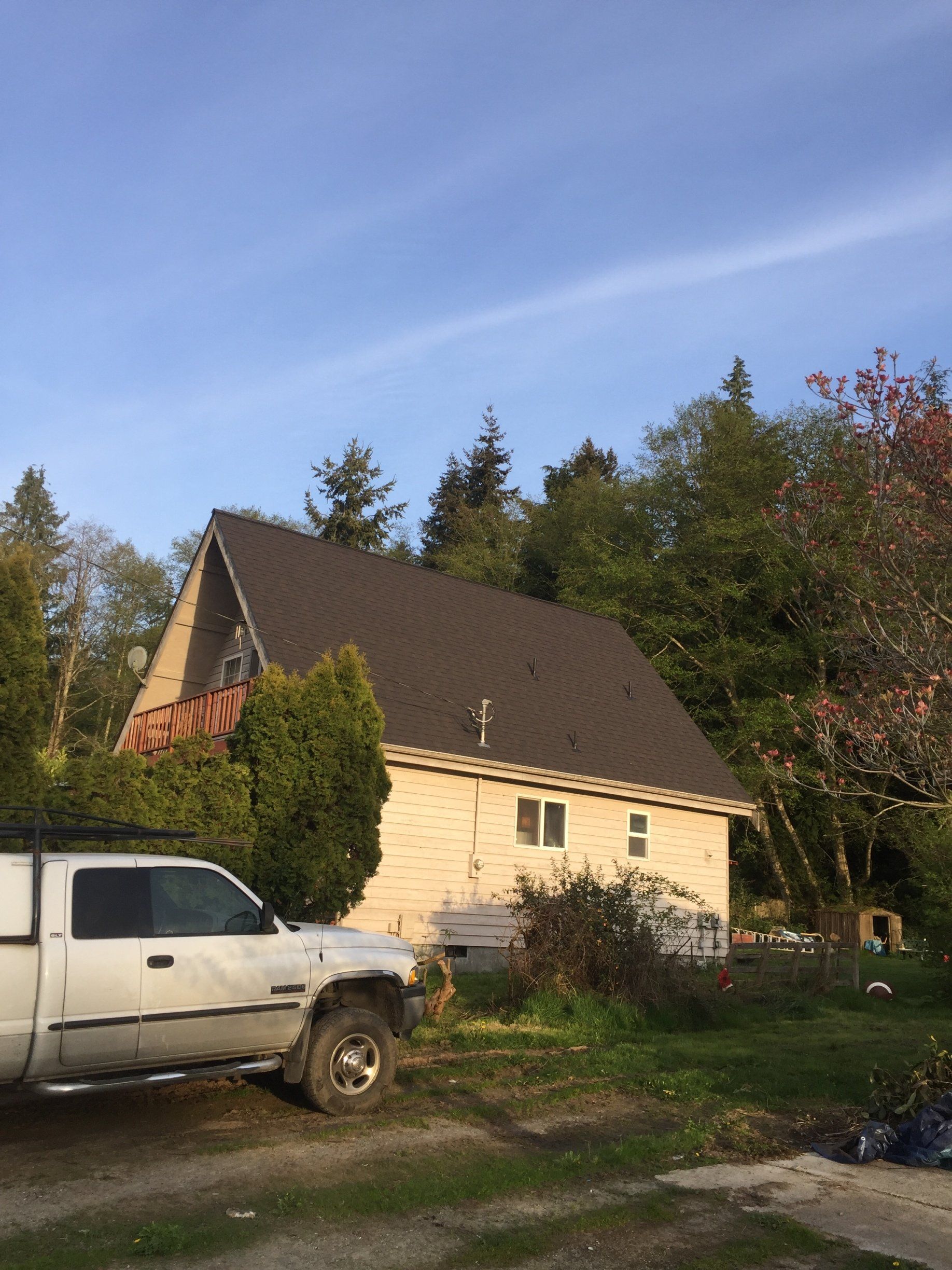 White house with steep dark roof, partly obscured by trees, beside an old white pickup truck under a blue sky.