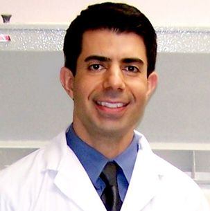 A man in a lab coat and tie smiles for the camera
