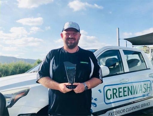 A man is holding an award in front of a greenwash truck.