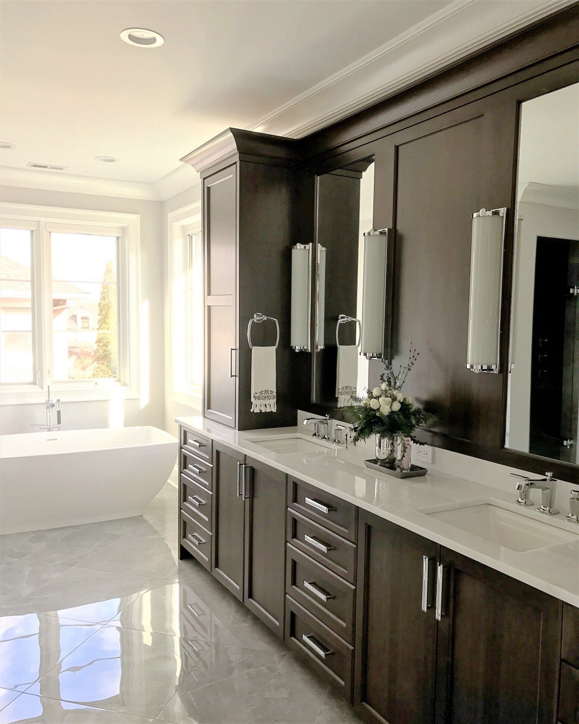 A bathroom with a tub , sink , mirrors and cabinets.