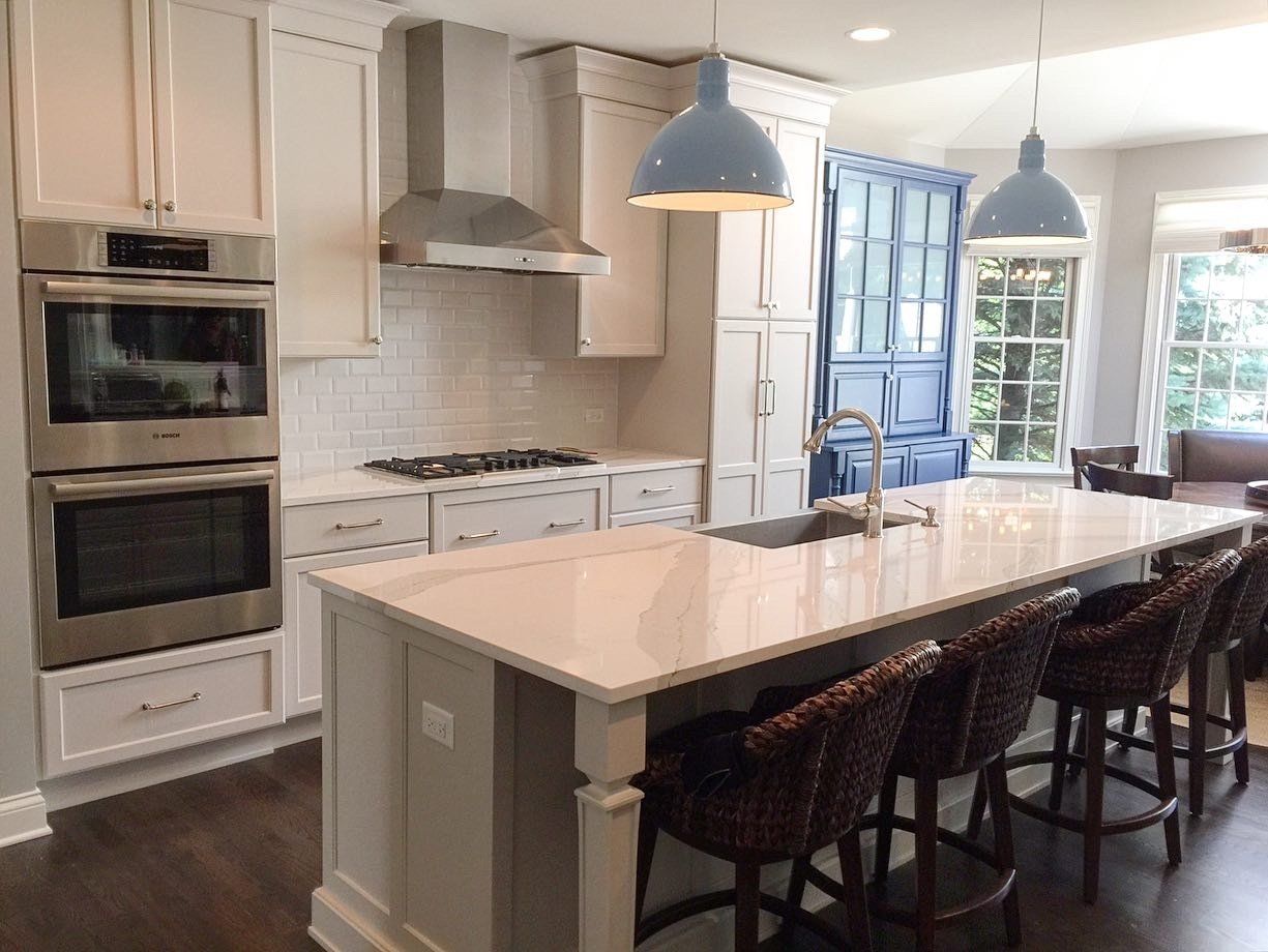 A kitchen with white cabinets , stainless steel appliances , a large island and wicker chairs.