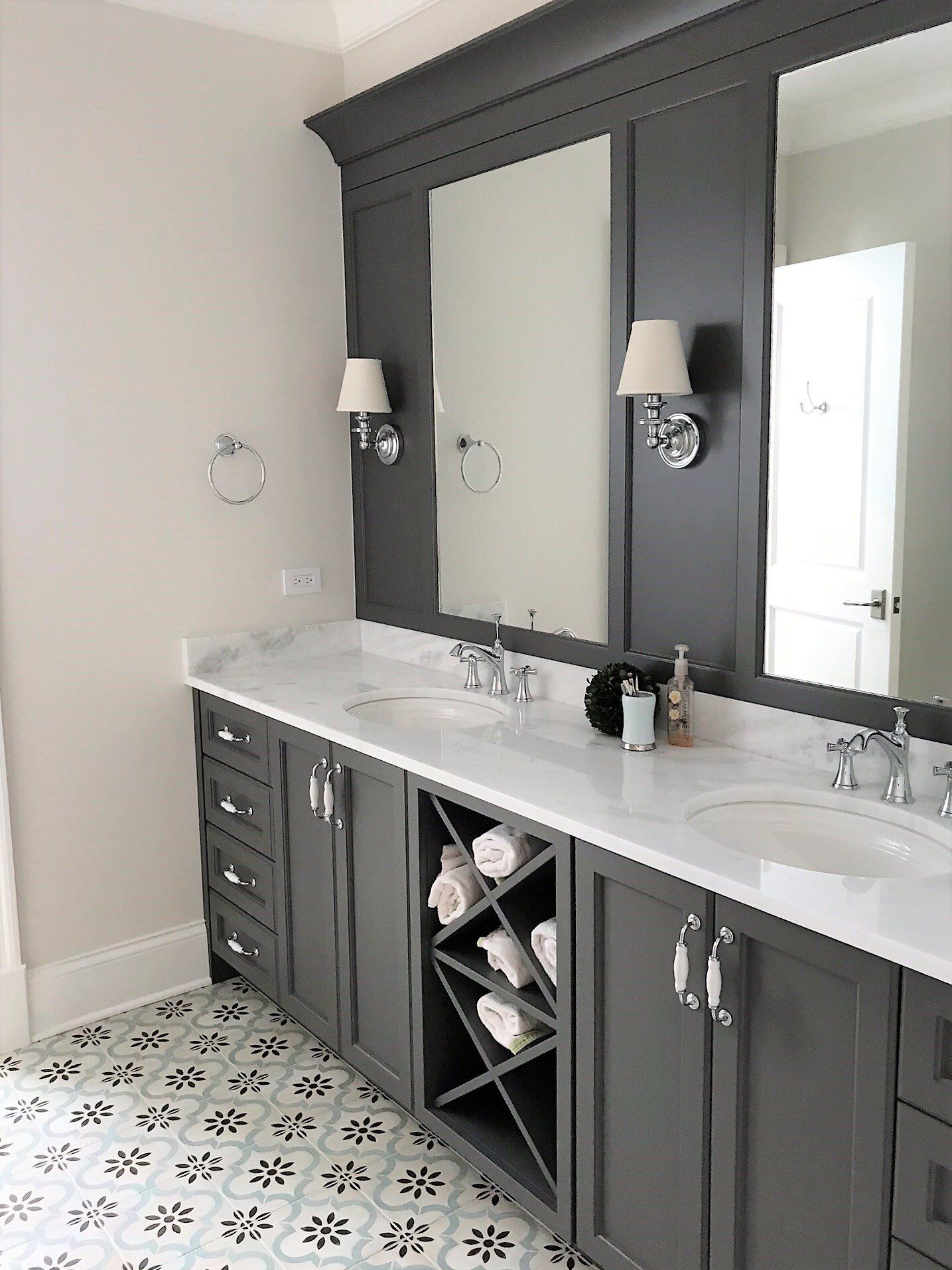 A bathroom with two sinks , two mirrors and a wine rack.