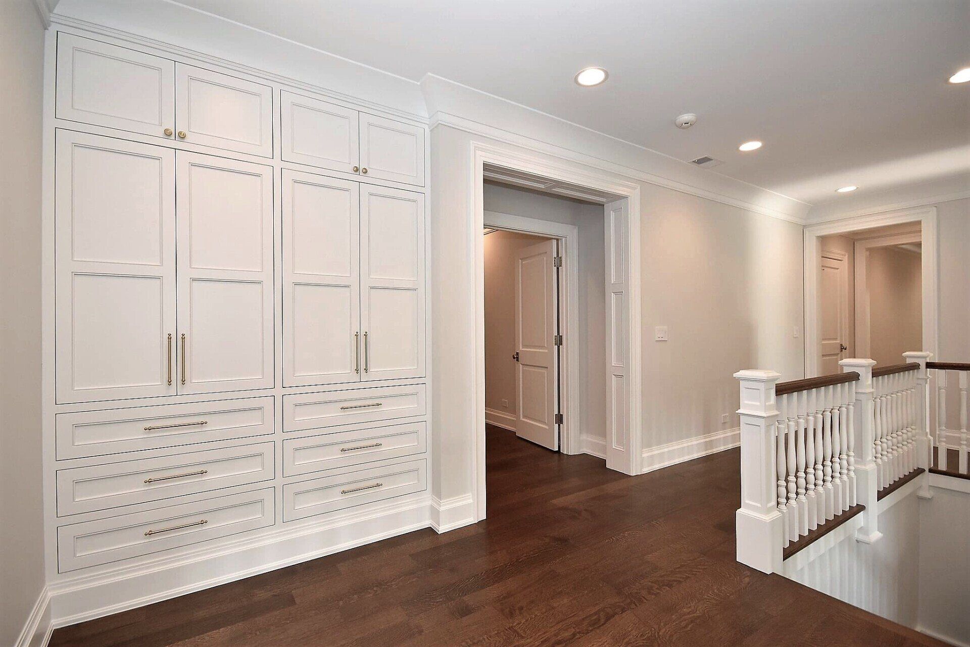 An empty hallway with white cabinets and wooden floors leading to a staircase.