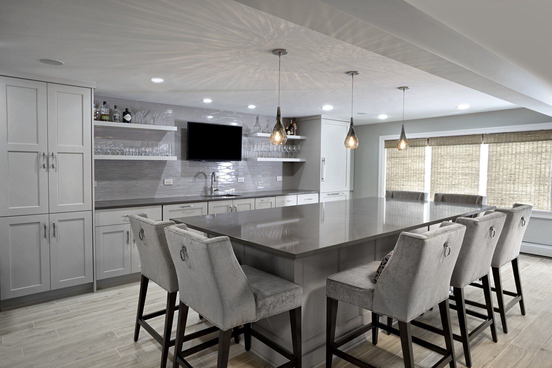 A kitchen with a large island and stools and a flat screen tv.