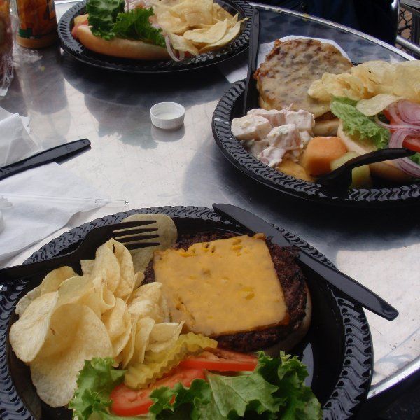 Borden met eten, waaronder een hamburger, hotdog en salade, op een metalen tafel met chips.