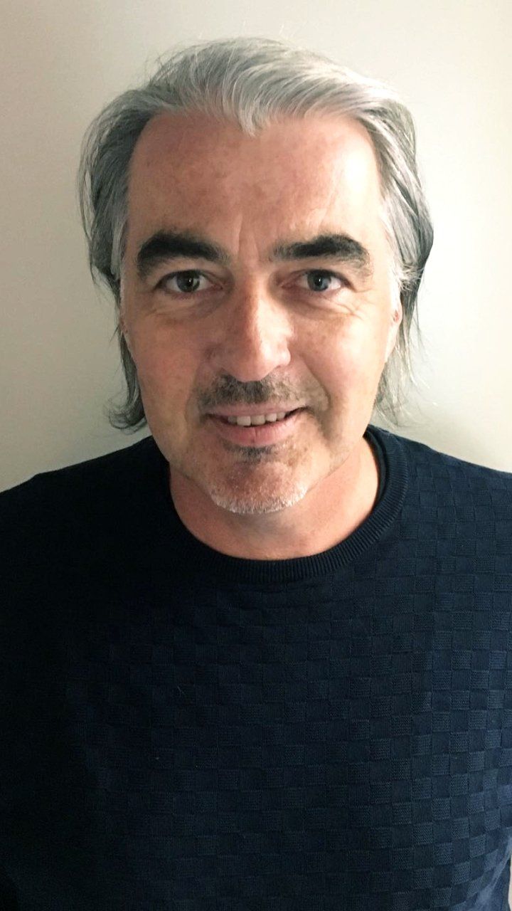 Ein Mann mit ergrauendem Haar und blauem Pullover lächelt in die Kamera.