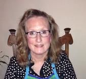 A woman wearing glasses and an apron is sitting in a chair.