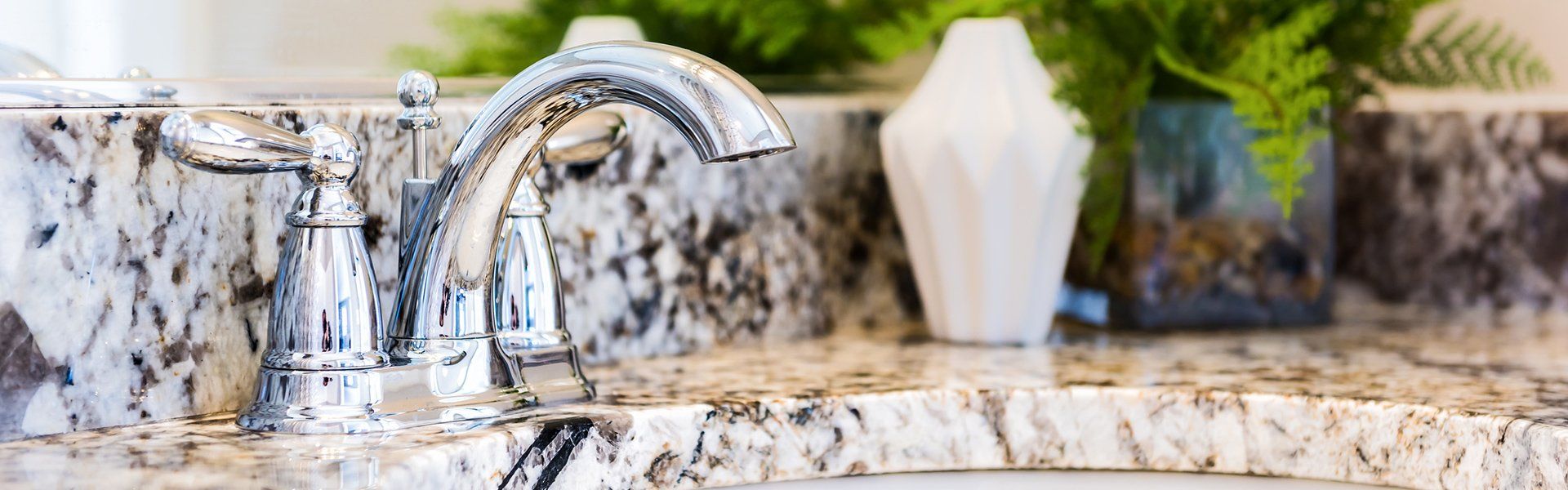 A bathroom sink with a faucet and a vase on the counter.