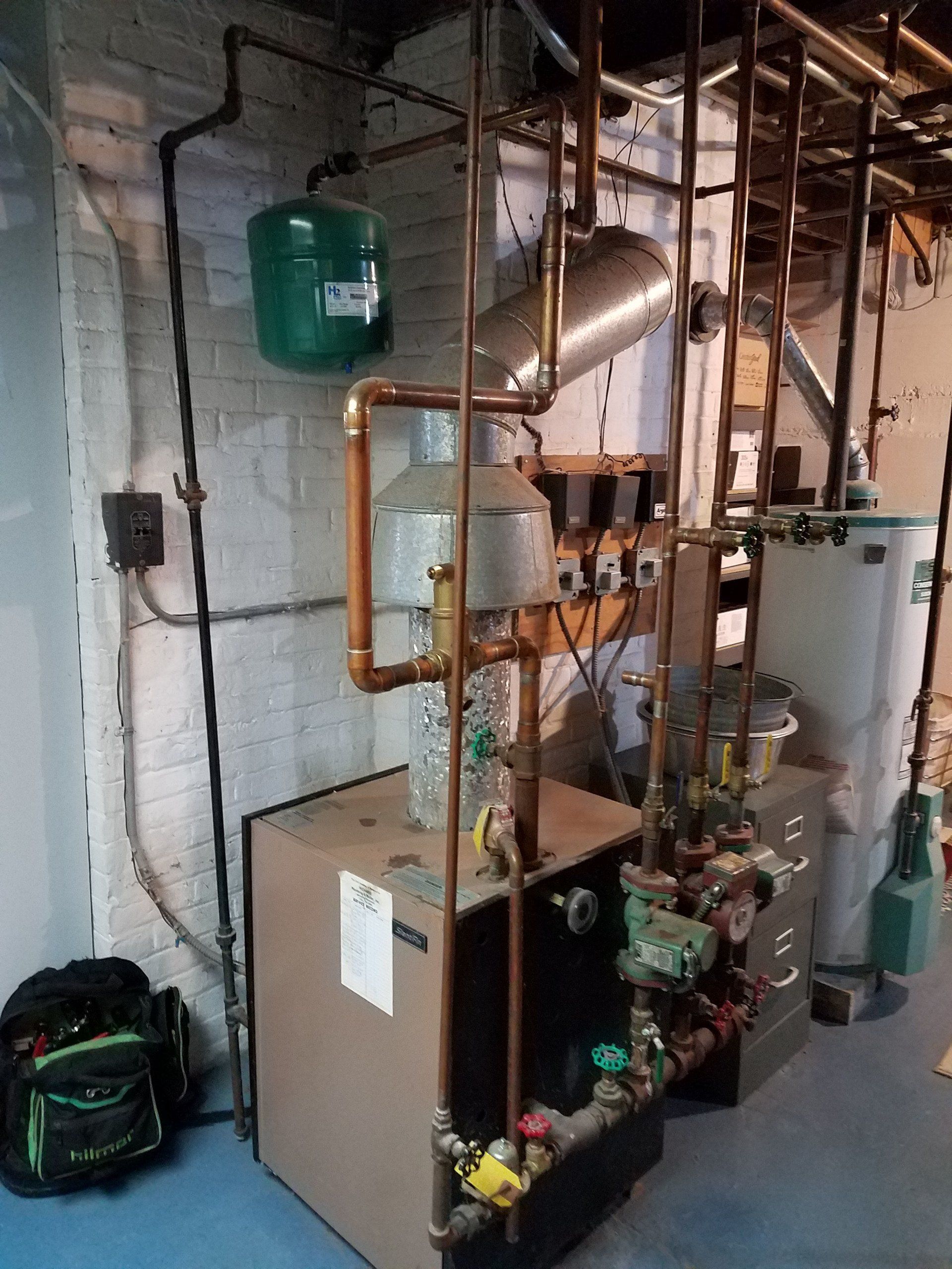 Industrial boiler and copper piping in a basement utility room with a green expansion tank.