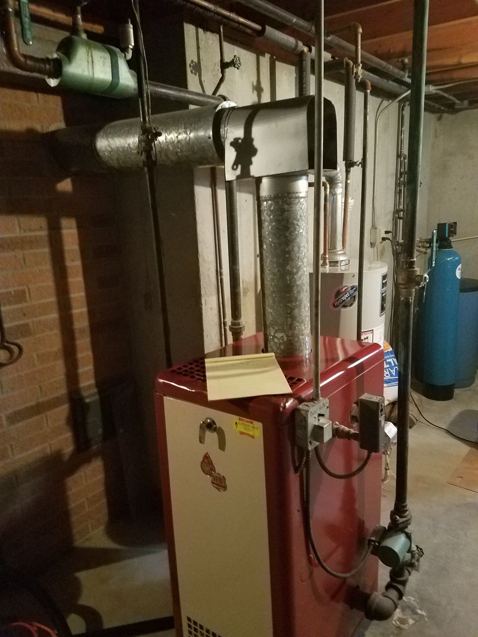 Basement furnace with red and cream boiler, metal vent piping, and blue water tank against cinderblock walls