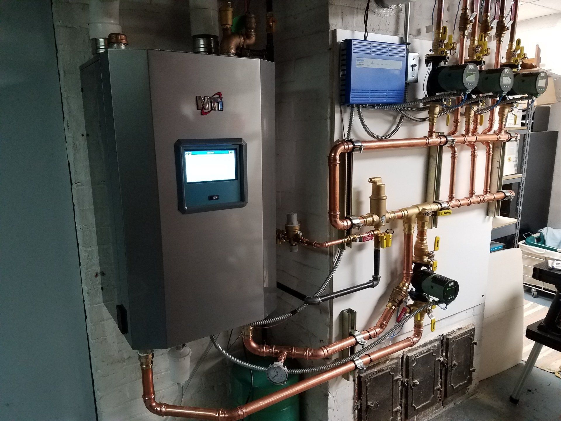 Industrial HVAC/mechanical room with wall-mounted control panel and copper piping on a white wall