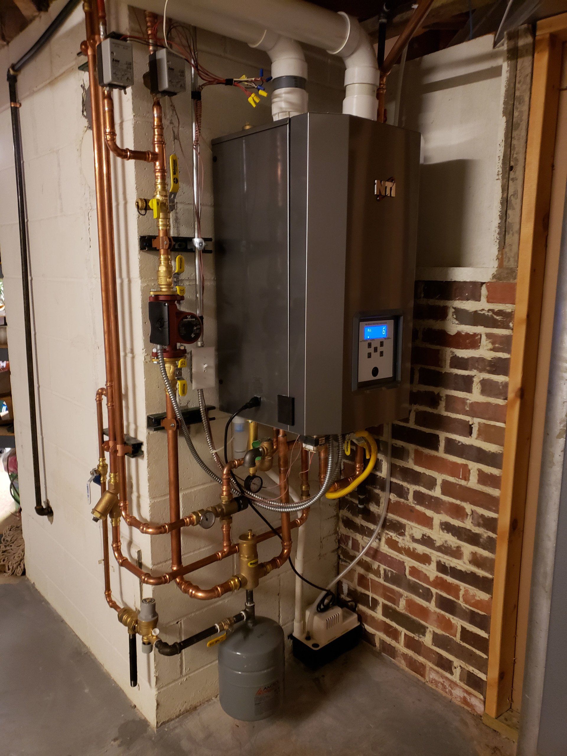 Wall-mounted boiler and pipes in a utility room with exposed brick wall.