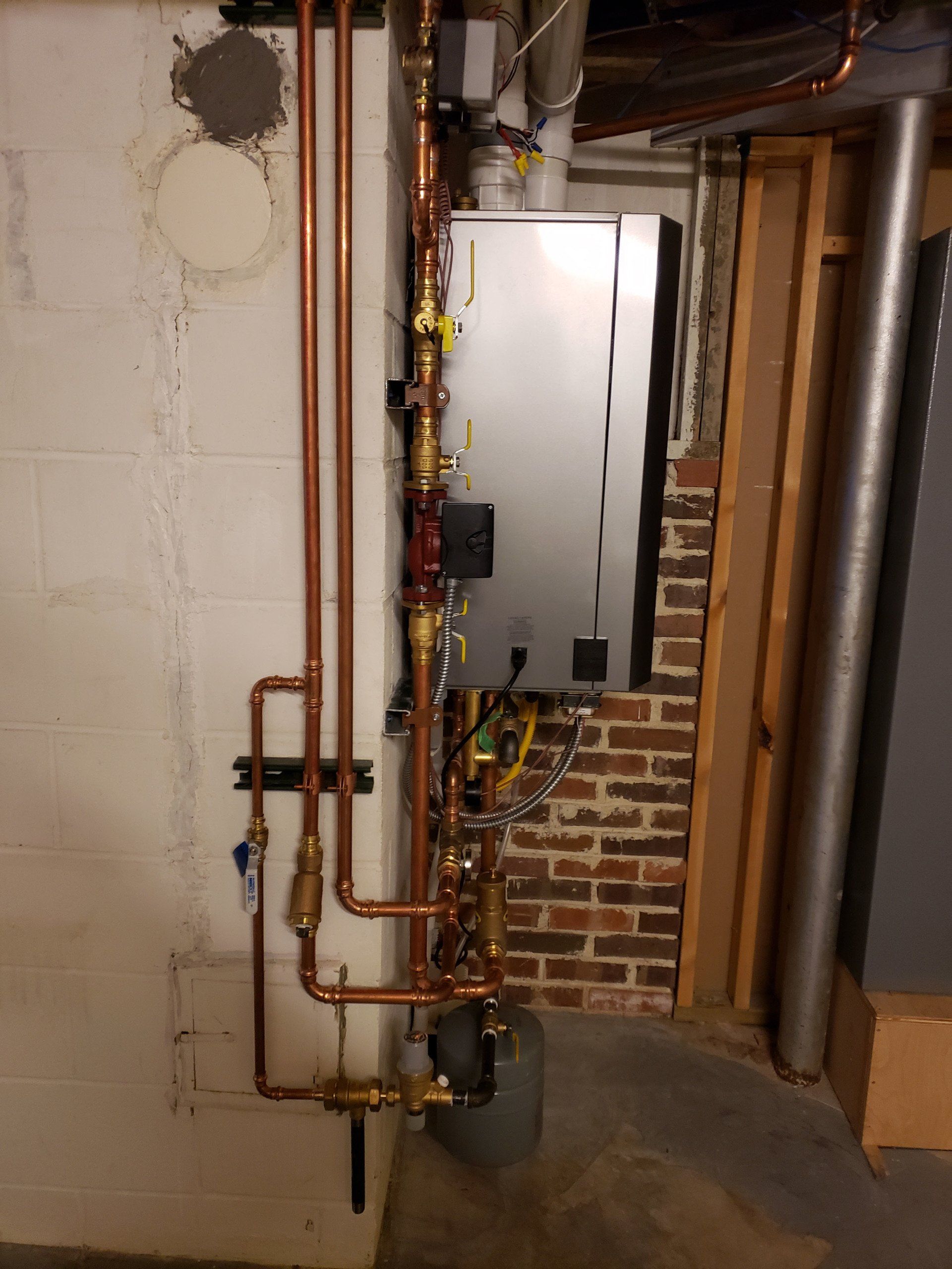 Basement utility area with exposed copper plumbing pipes and a metal furnace or boiler panel on a brick wall