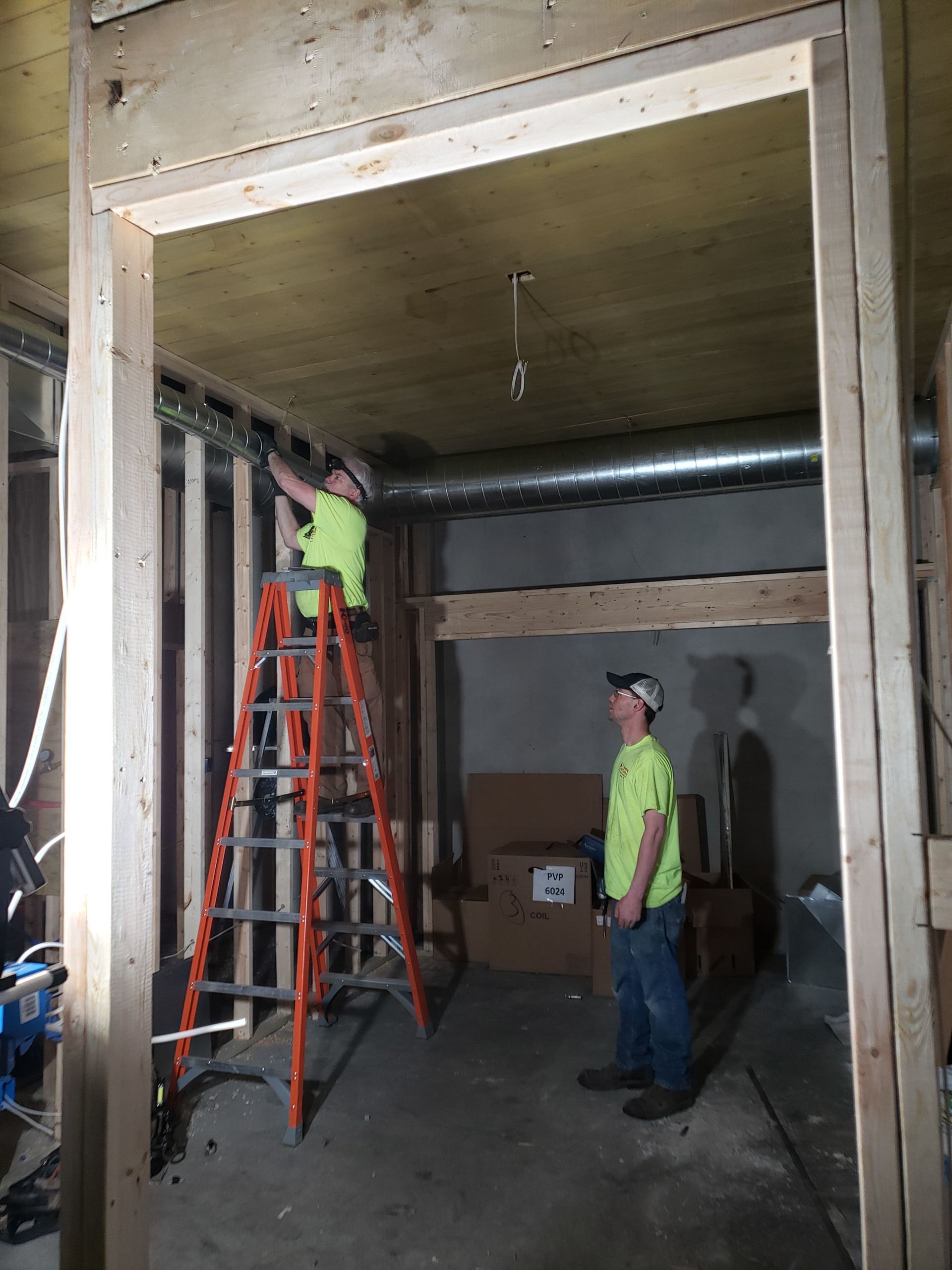 Workers on red and black ladders inside an unfinished industrial doorway, one installing overhead work