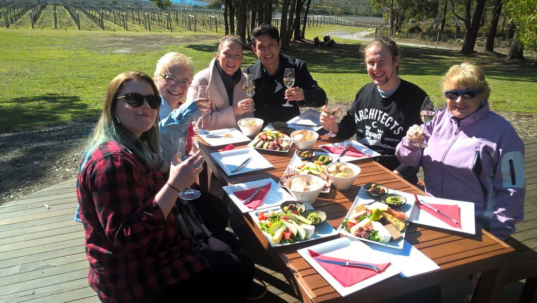 A family enjoying lunch together outdoors, with glasses of wine on the table.