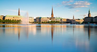 Die Skyline einer Stadt spiegelt sich im Wasser eines Sees.