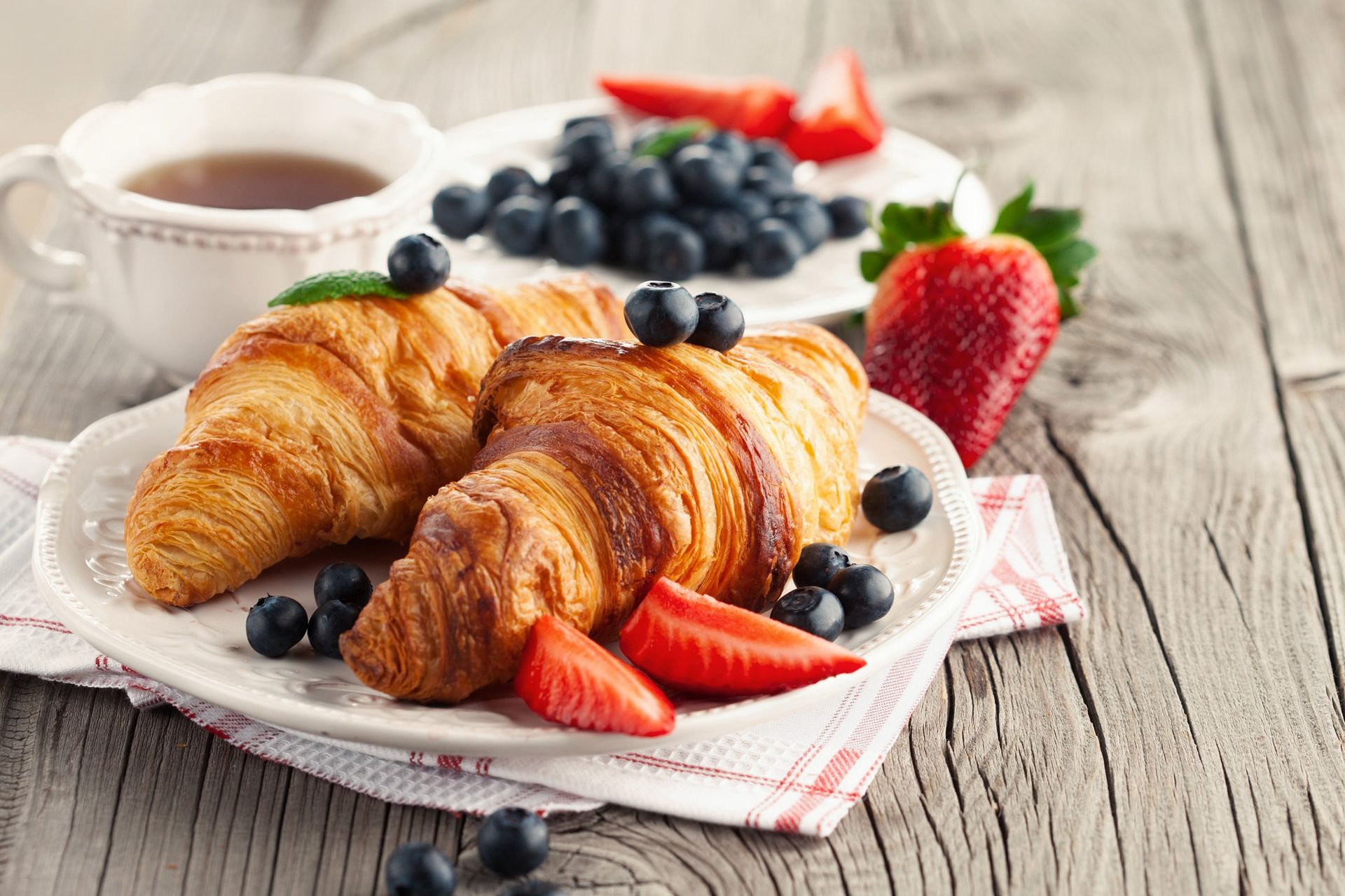 Zwei Croissants mit Erdbeeren und Blaubeeren auf einem Teller auf einem Holztisch.