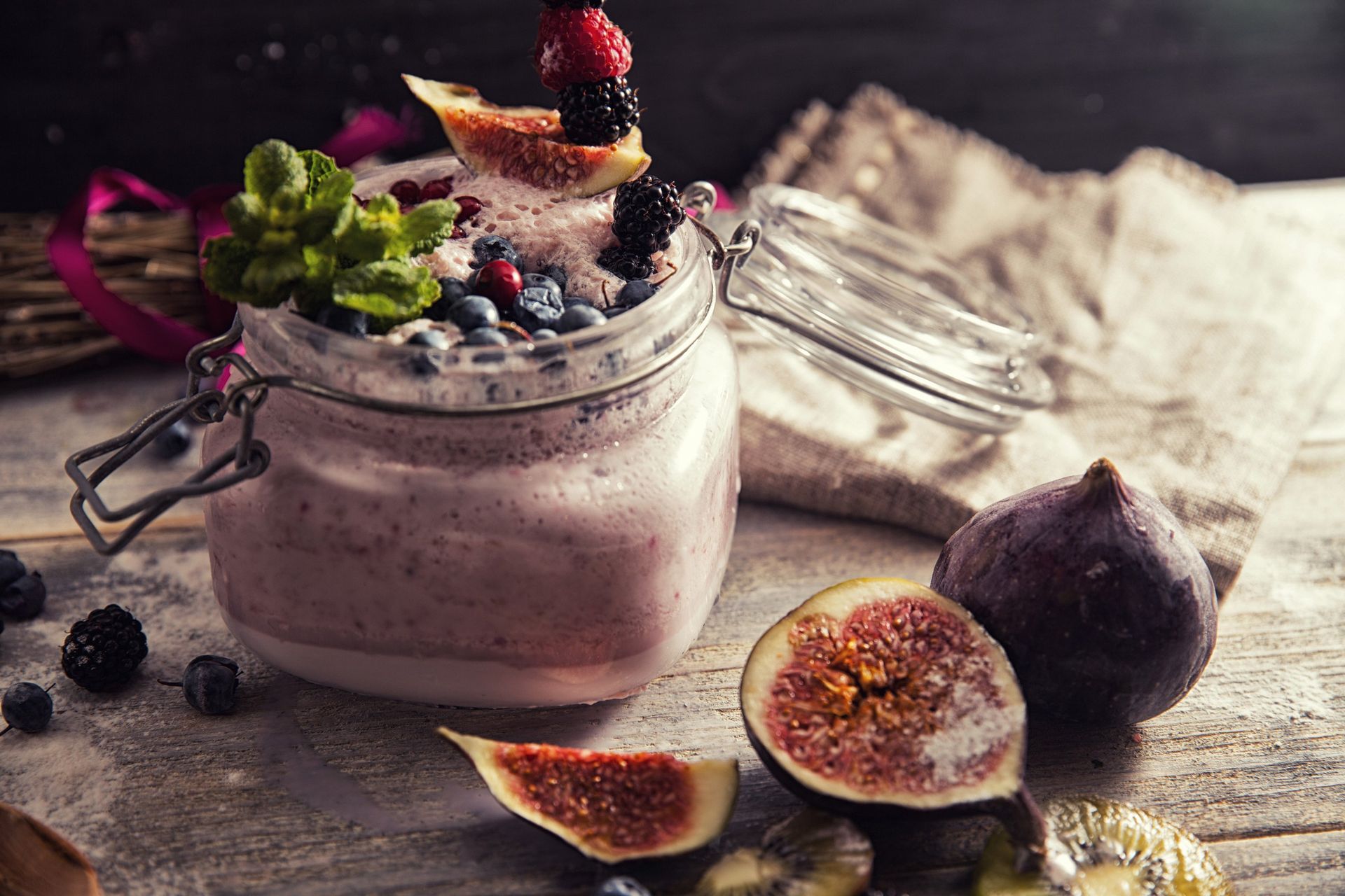 Ein Glas Joghurt mit Beeren und Feigen auf einem Tisch.