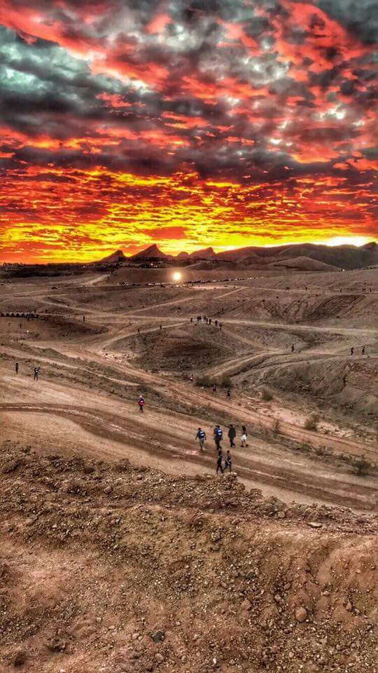 A group of people standing on top of a dirt hill at sunset.