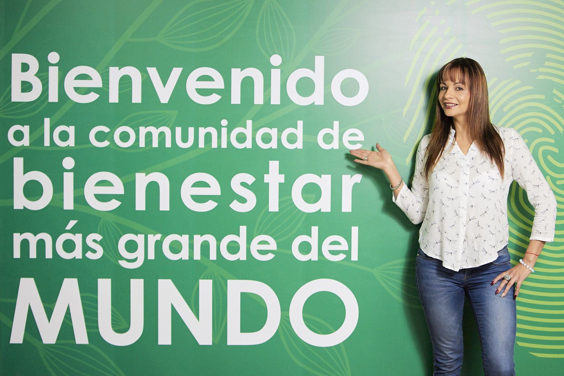 Texto en español con Carolina Ucrós de pie sobre fondo verde: “Bienvenido a la comunidad de bienestar más grande del mundo”.
