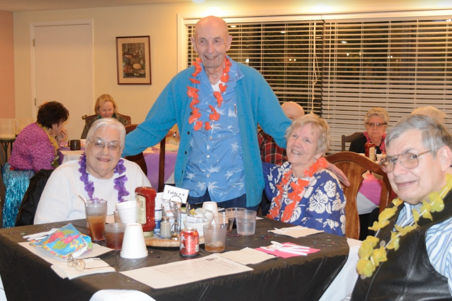 Group of seniors at a Hawaiian-themed event, wearing leis, smiling at the camera.