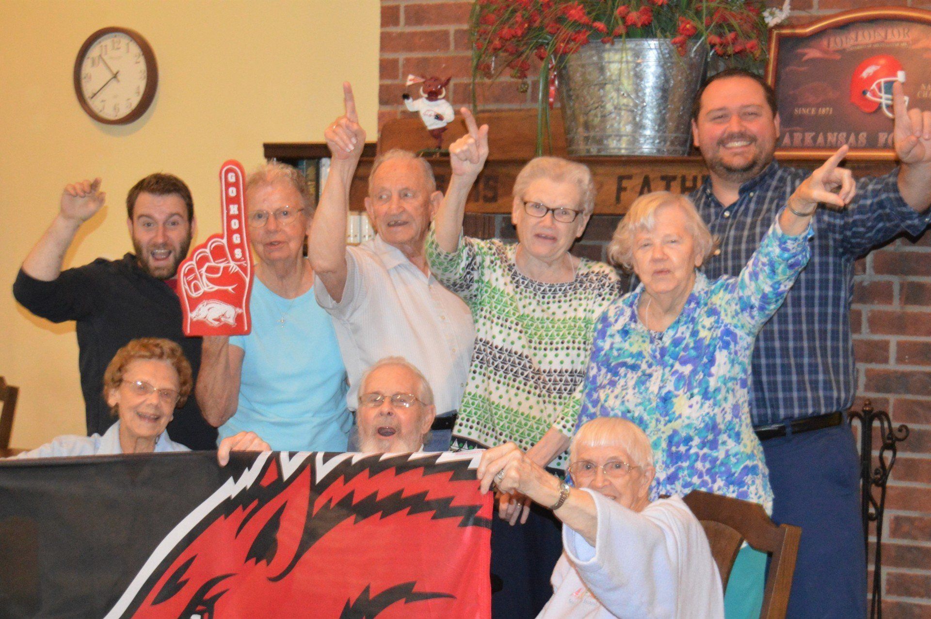 Group of people cheering, holding a Razorbacks flag and foam finger, indoors.