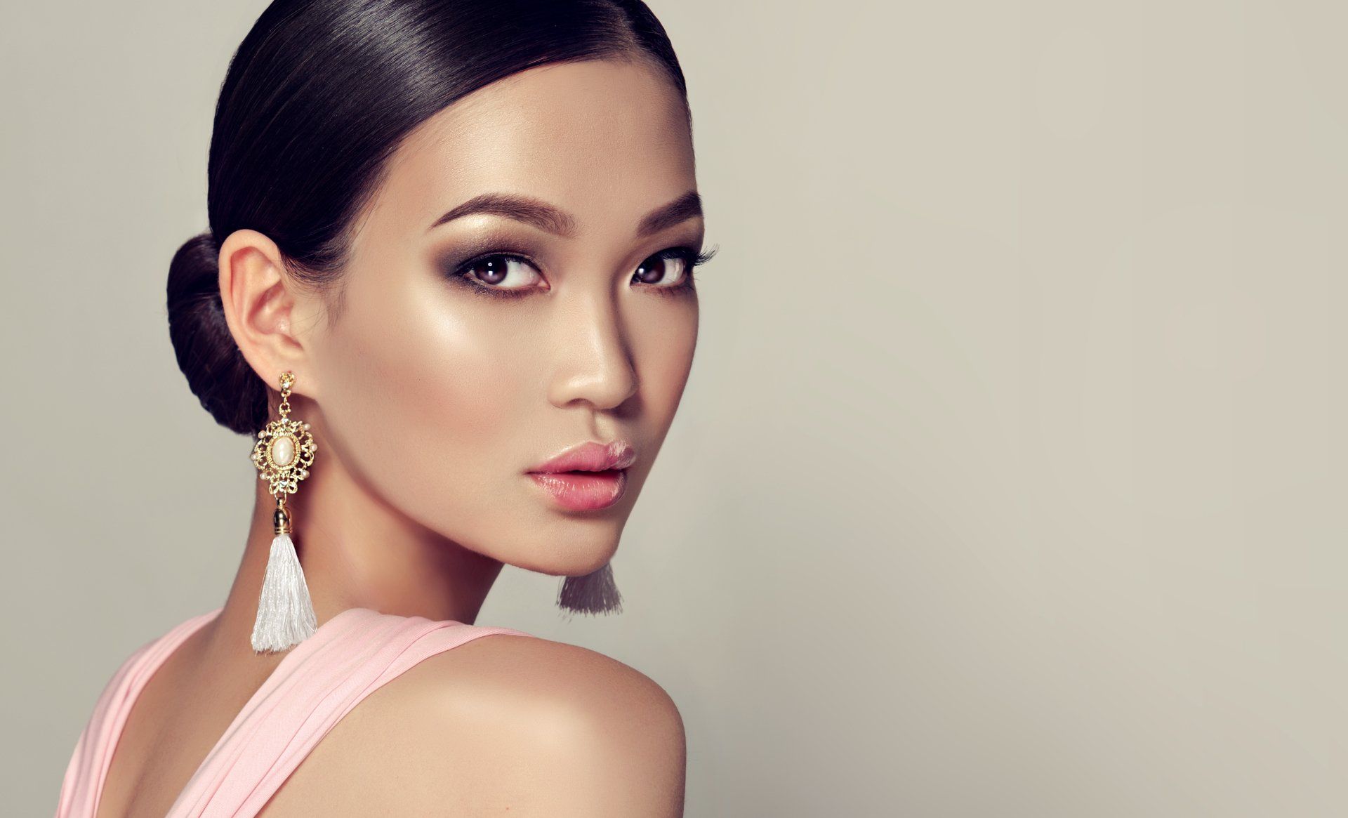 A woman in a pink dress and earrings is looking over her shoulder.