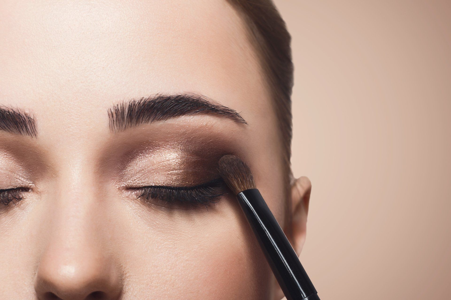 A woman is applying eye shadow to her eye with a brush.