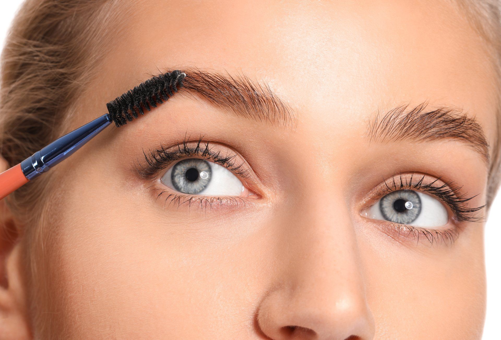 A woman is brushing her eyebrows with a brush.