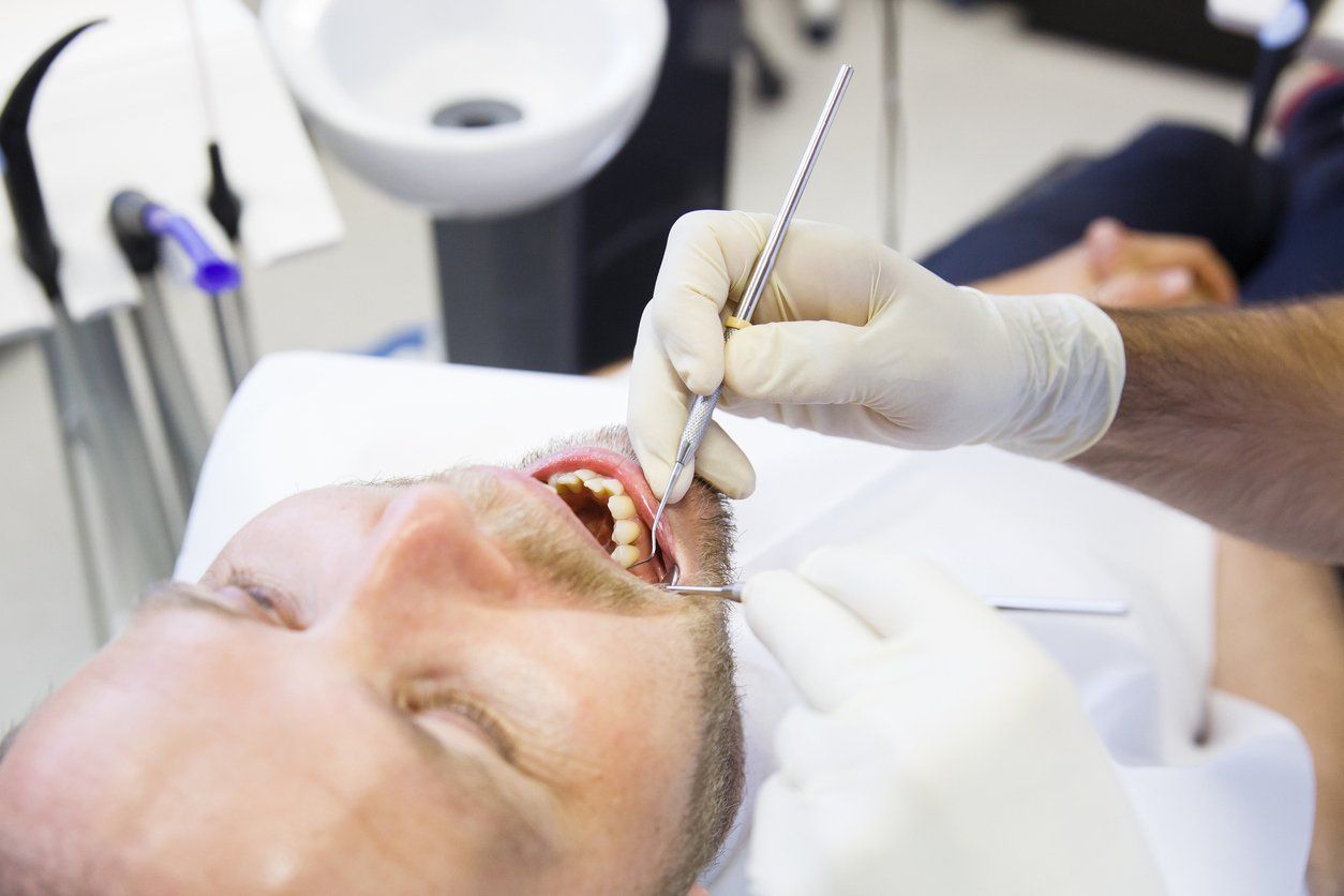 man-reclined-in-dentist-chair-while-dentist-looks-in-mouth