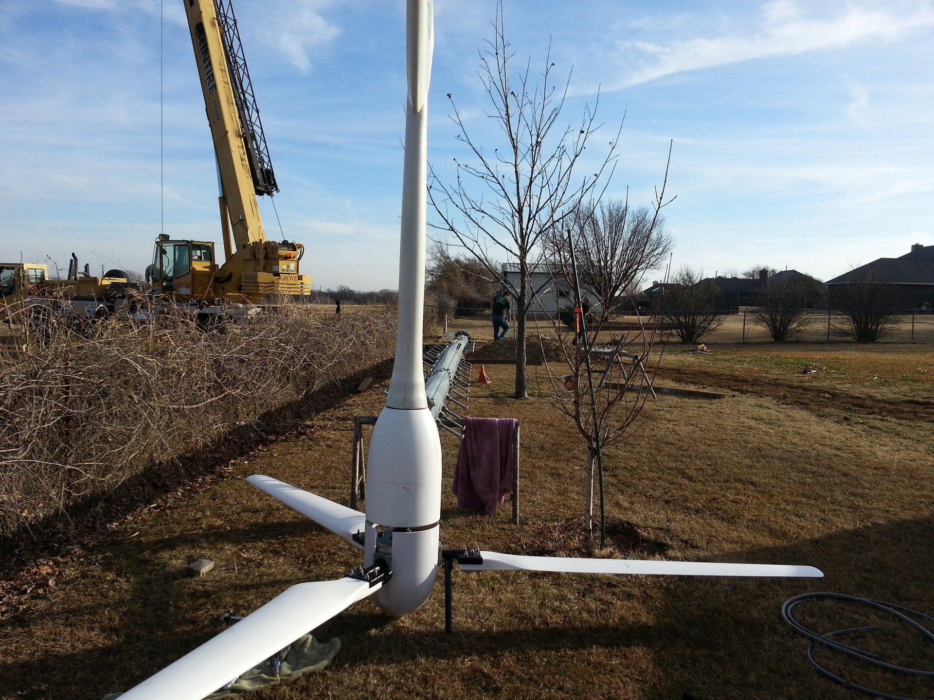 A wind turbine in a field with a crane in the background