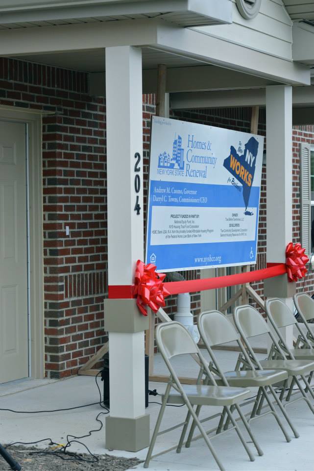 Ribbon-cutting ceremony at 204 building, with sign and chairs. Red bows on white columns, brick exterior.