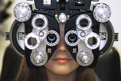 Woman's Face Behind Eye Test Equipment — Eye & Contact Lens Clinic in Bremerton, WA Woman's Face Behind Eye Test Equipment — Eye & Contact Lens Clinic in Bremerton, WA