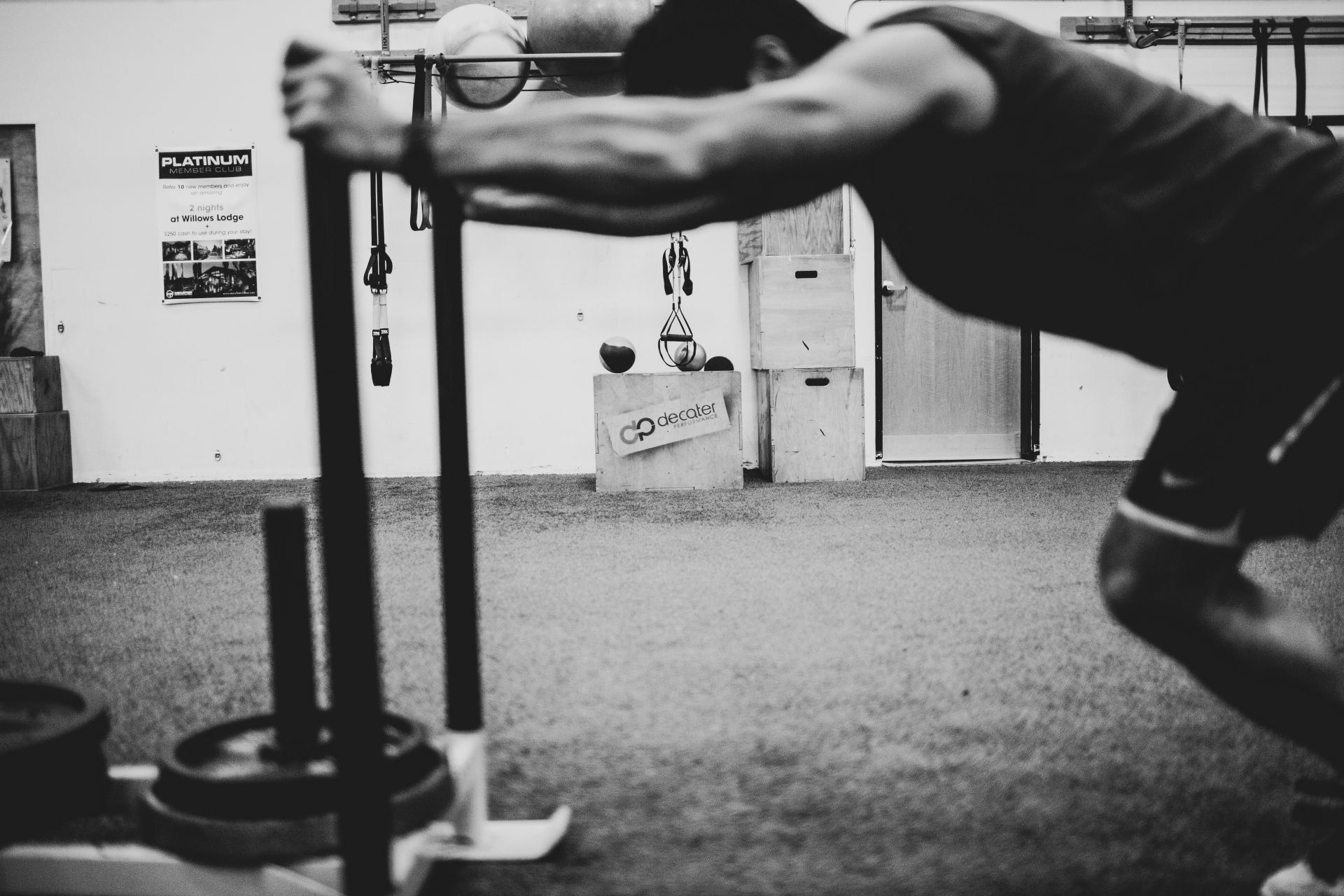 Man pushing a weighted sled in a gym. Black and white photo.