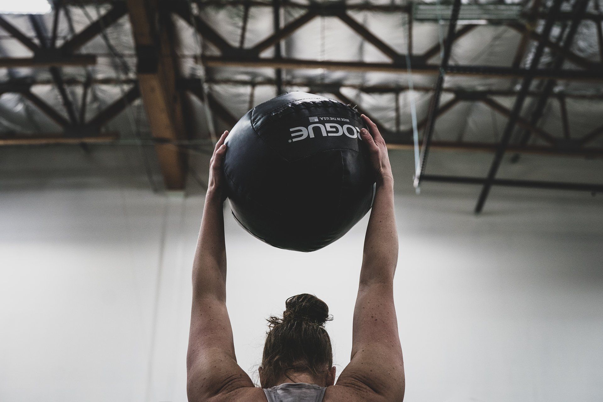 Woman holding a black medicine ball above her head in a gym.