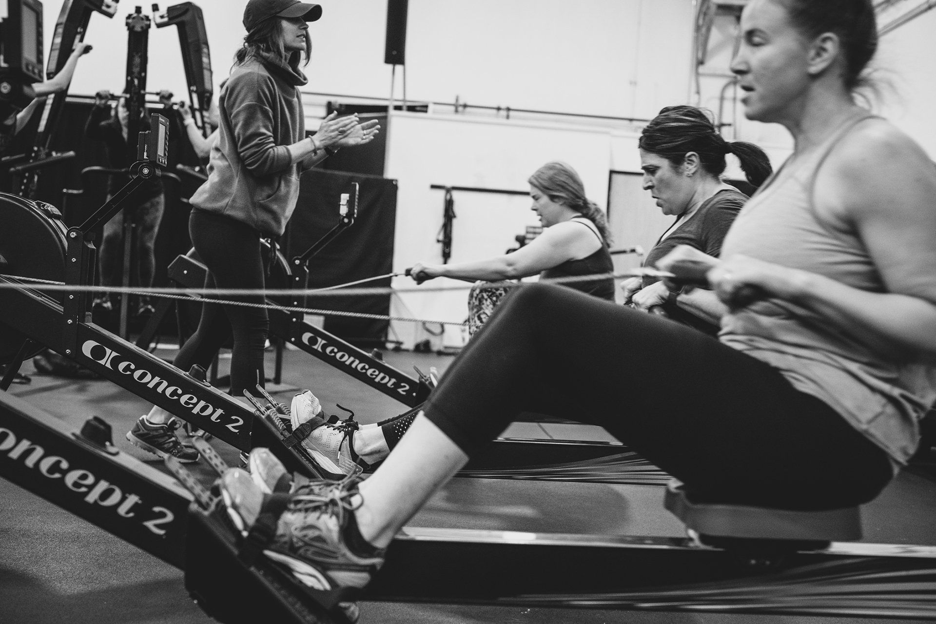 People rowing on Concept2 machines in a gym, instructor giving guidance.