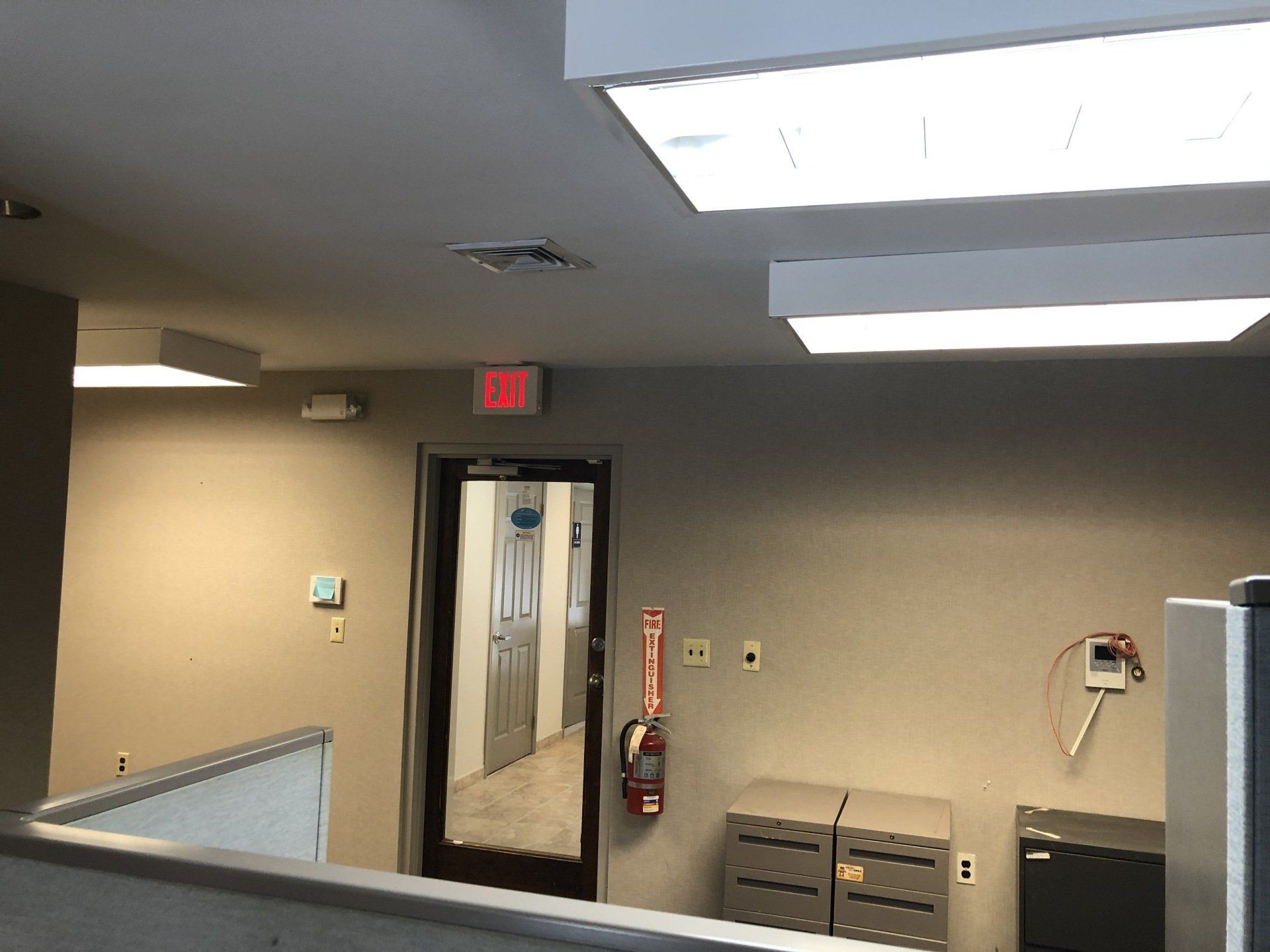 Interior office view with door, exit sign, fire extinguisher, and overhead lights.