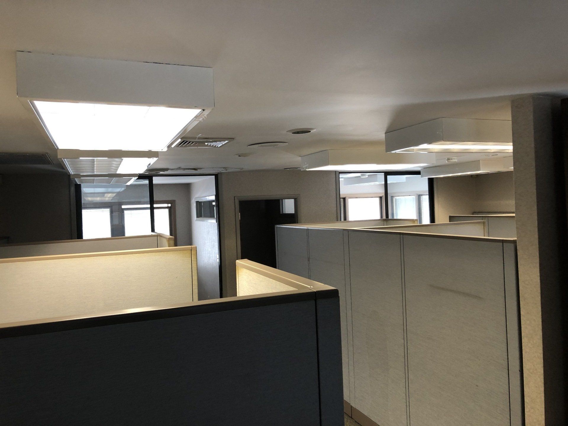 Office cubicles under bright fluorescent lights; view through the open space.