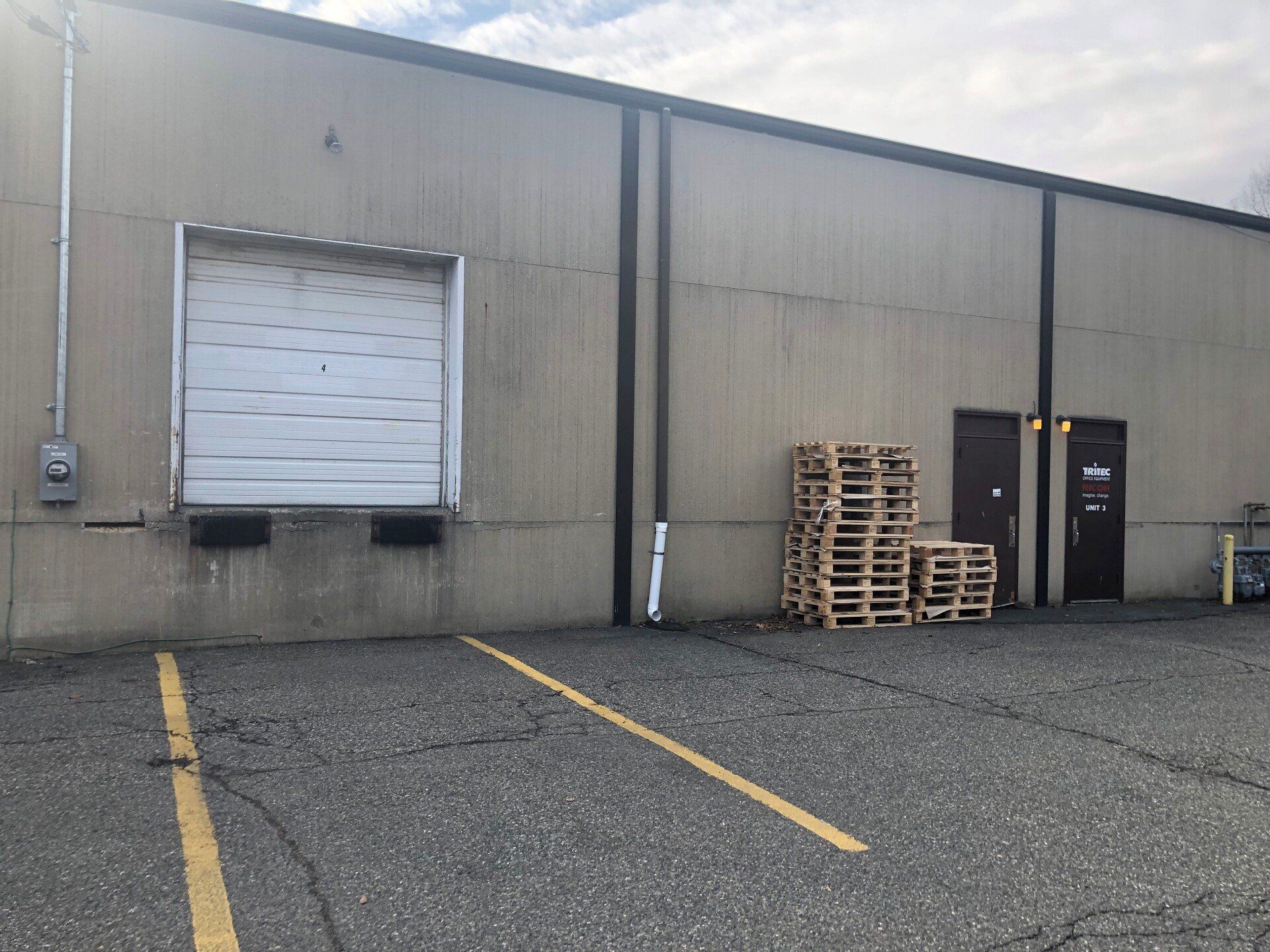 Exterior view of a commercial building with a loading dock, doors, and stacked pallets.