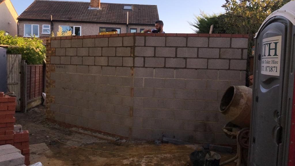 A portable toilet is sitting in front of a brick wall.