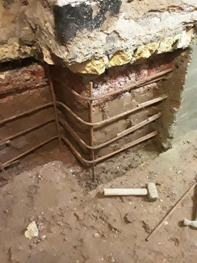 A hammer is laying on the ground next to a brick wall.