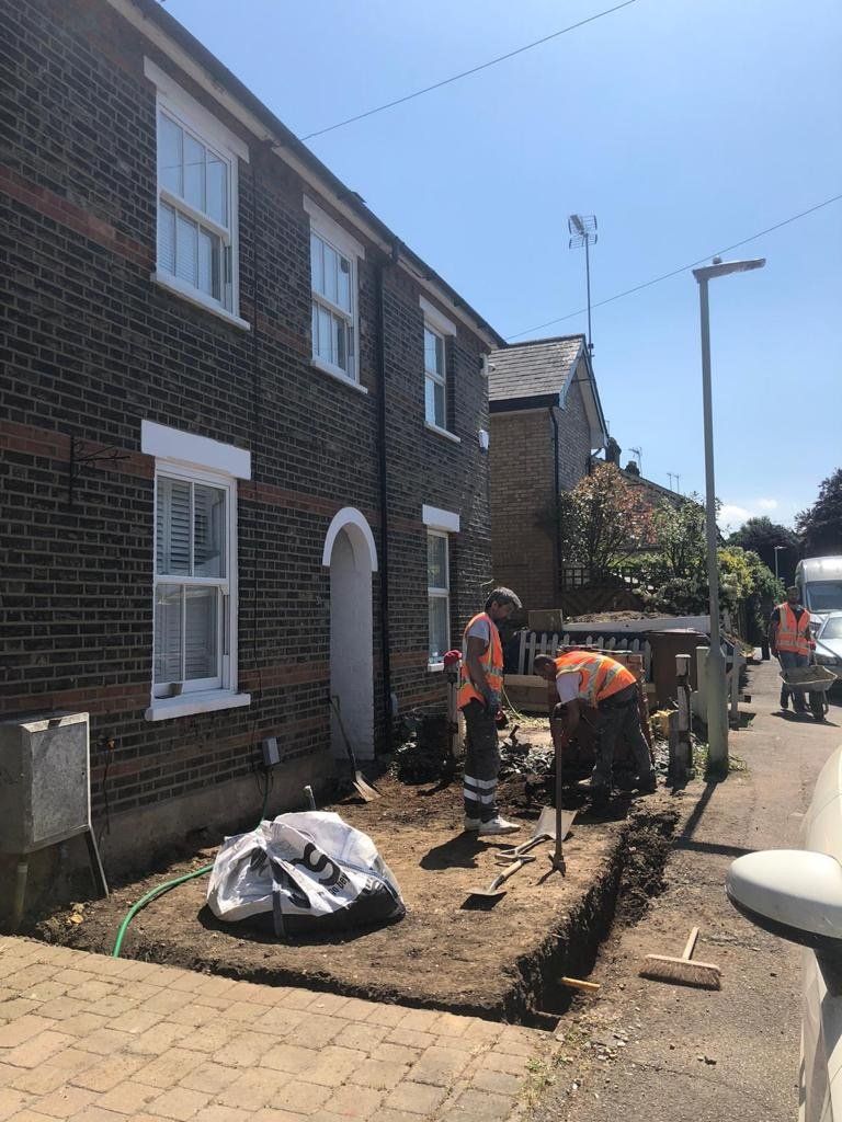 A group of construction workers are working on a sidewalk in front of a brick building.