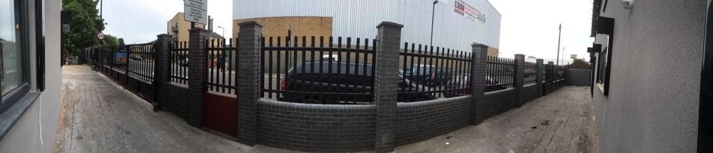 A fence surrounds a building with a lot of cars parked in front of it.