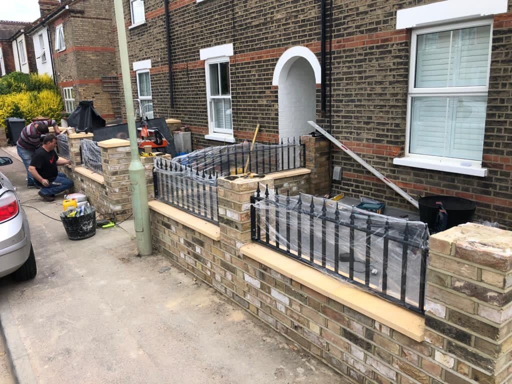 A man is working on a brick wall in front of a house.