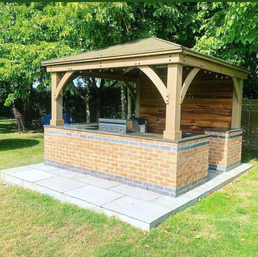 A brick gazebo with a wooden roof and a grill underneath it.