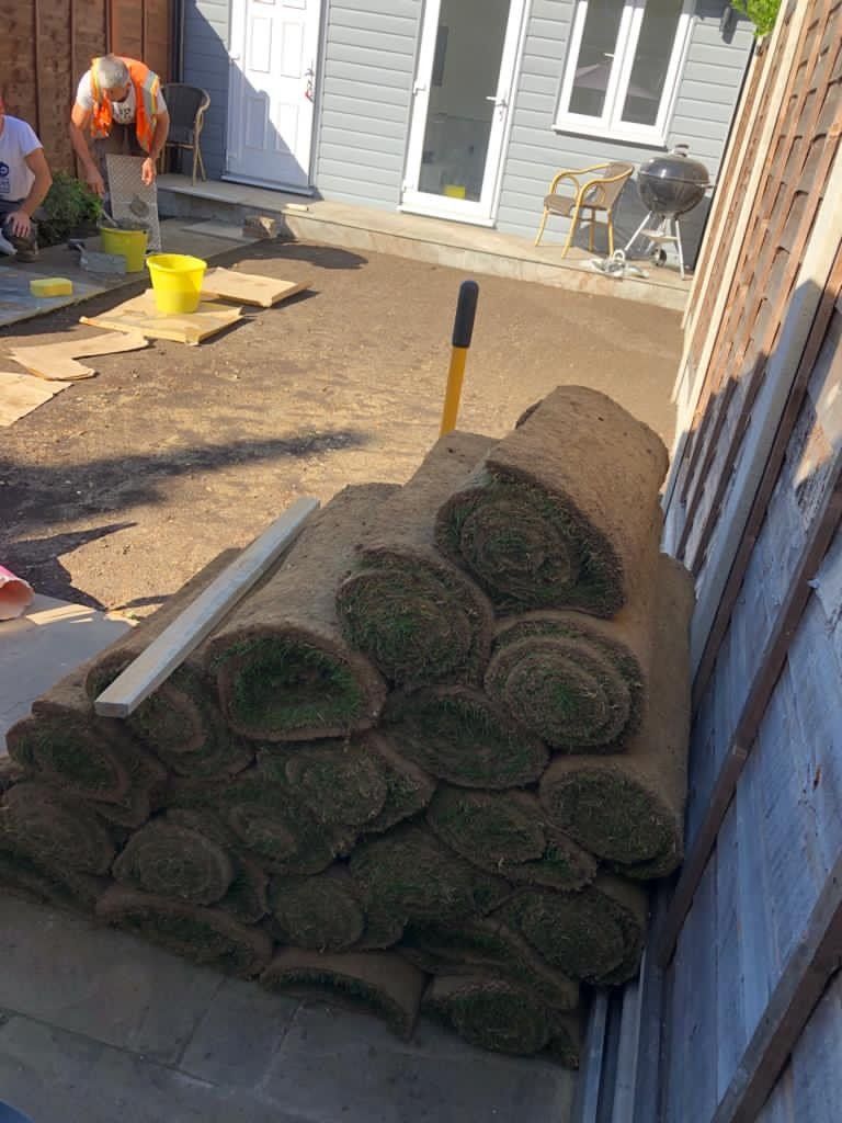 A pile of rolls of grass is sitting on the ground in front of a house.