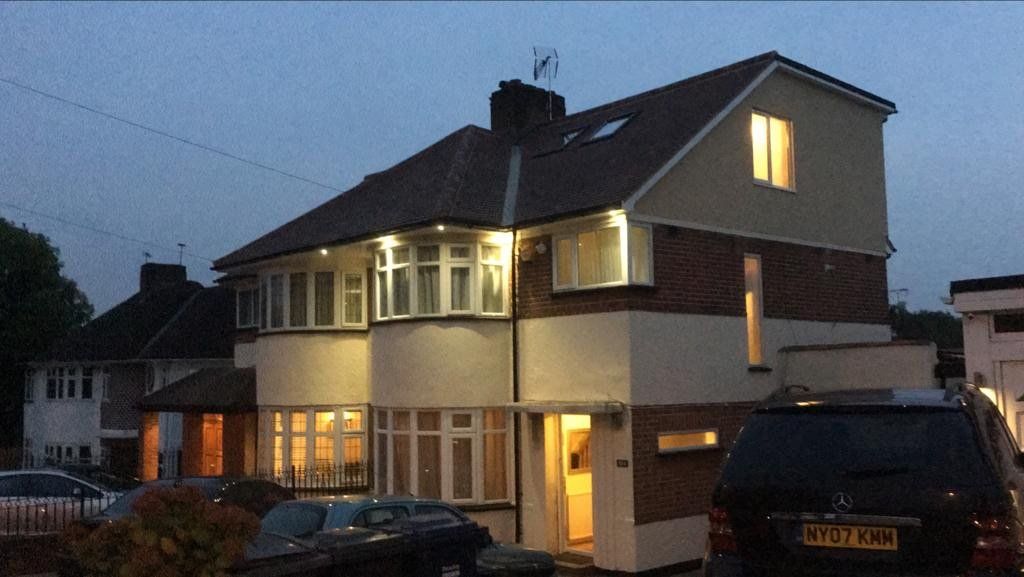 A car is parked in front of a house that is lit up at night.